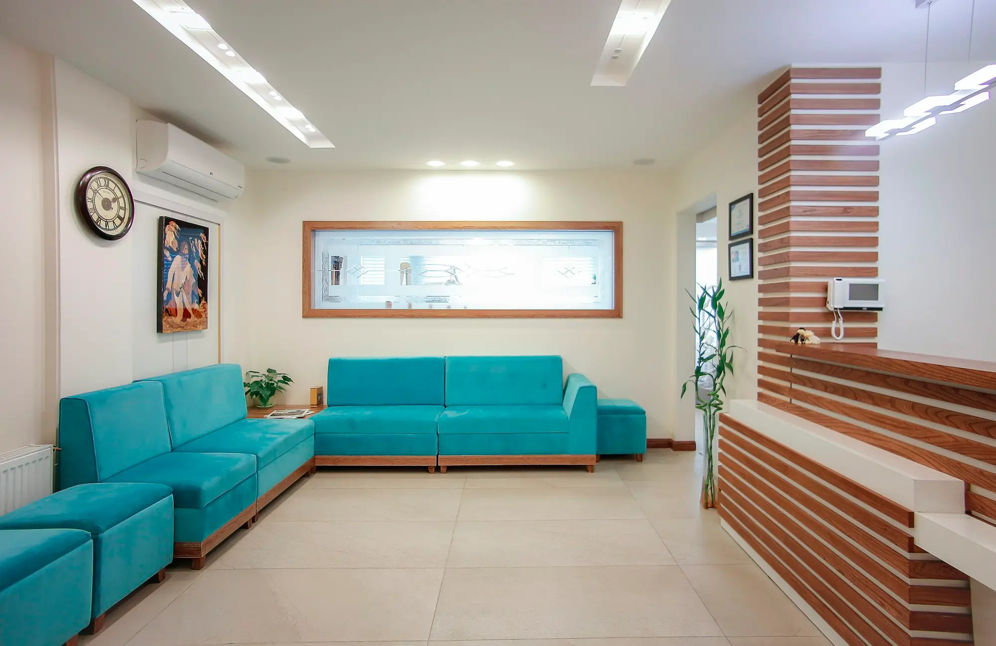 Clean, modern dental clinic reception with practice manager at computer, treatment room visible
