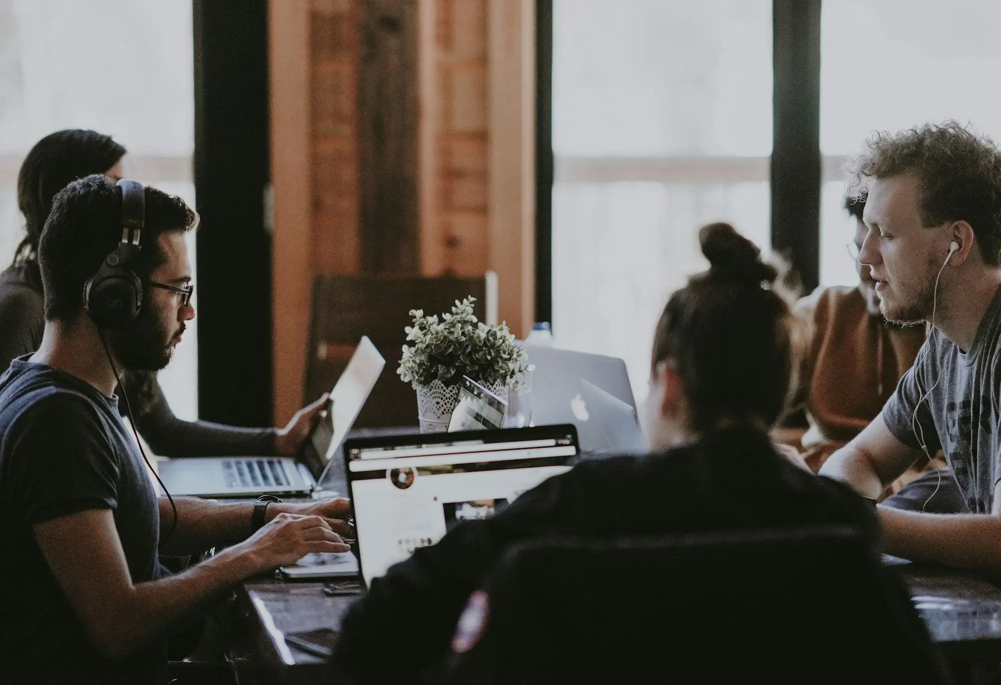 Small creative/digital agency team of three around a table with laptops and a large screen in a brick warehouse studio